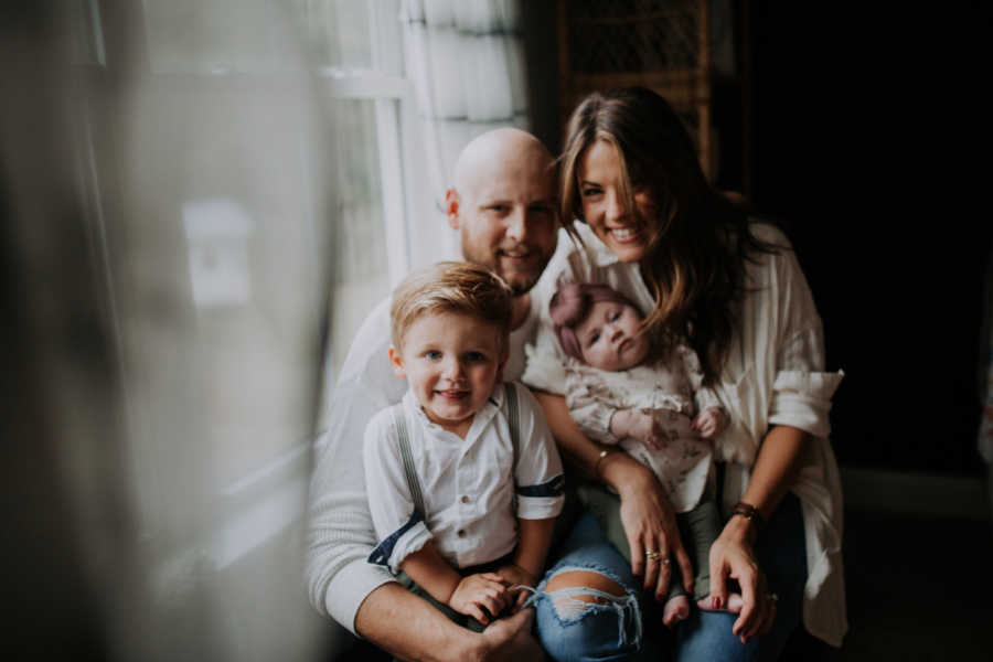 Husband and wife sits in home with their two adopted children in their laps