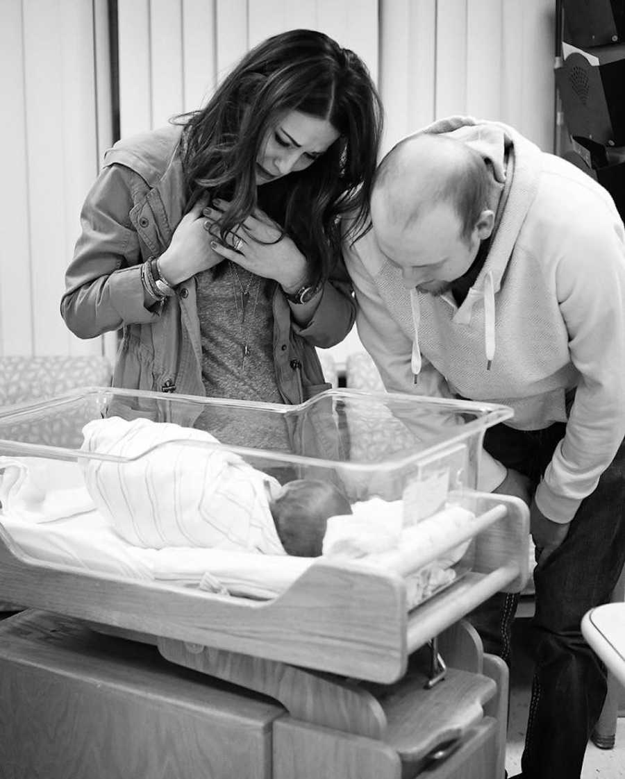 Husband and wife stand over sleeping newborn who they are adopting