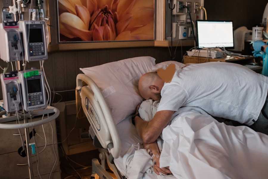 Father hugs woman in hospital bed who gave birth to his adopted child