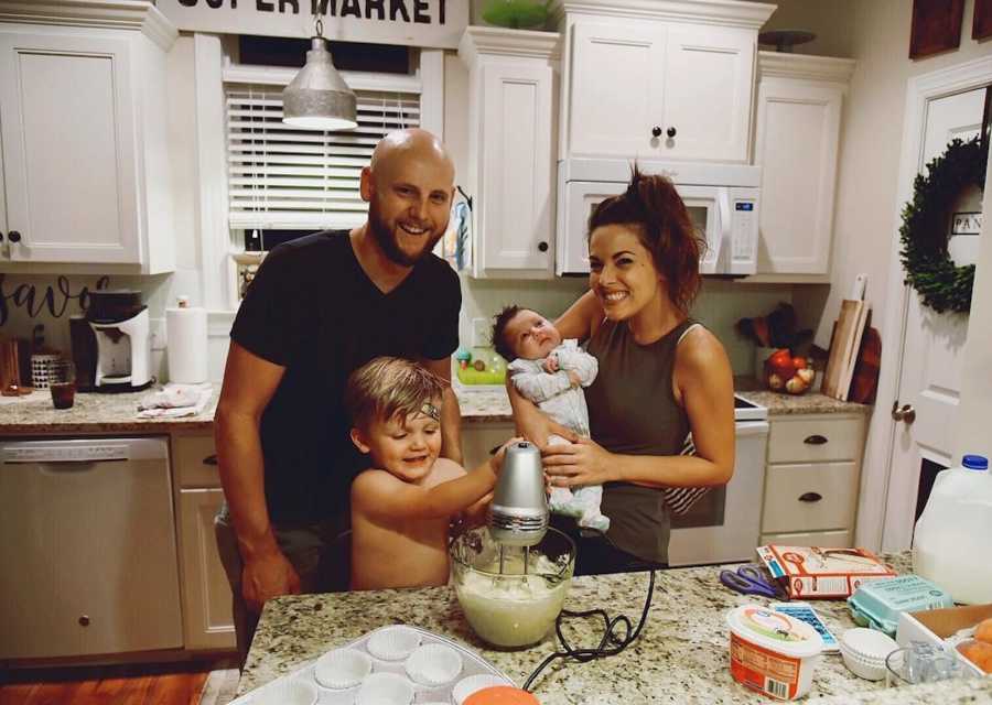 Husband and wife stand smiling in kitchen with their two adopted children
