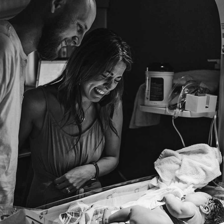 Husband and wife stands over newborn who they are adopting