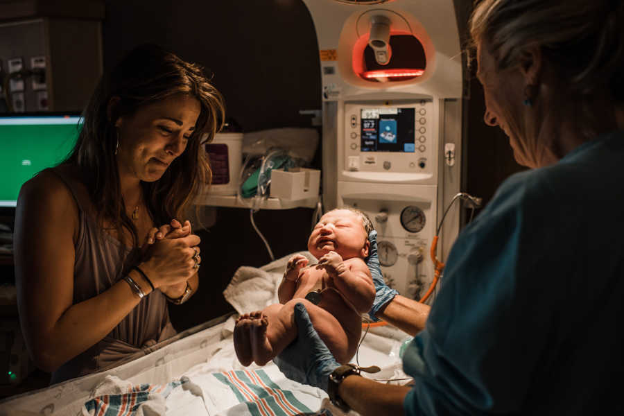Nurse stands in hospital room holding newborn as adoptive mother cries