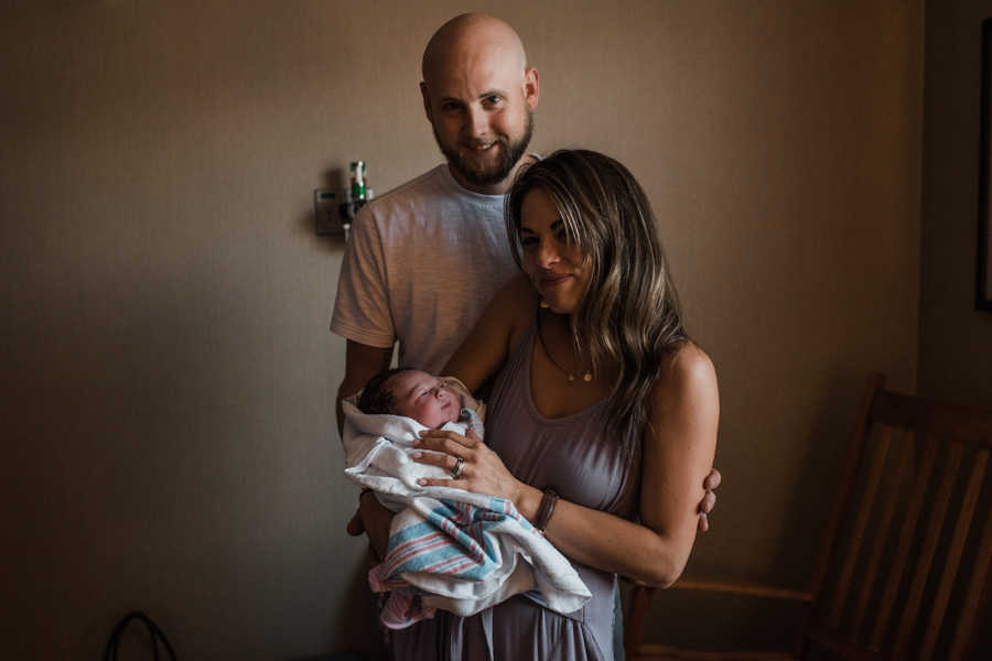 Husband and wife stand in hospital room holding adopted newborn