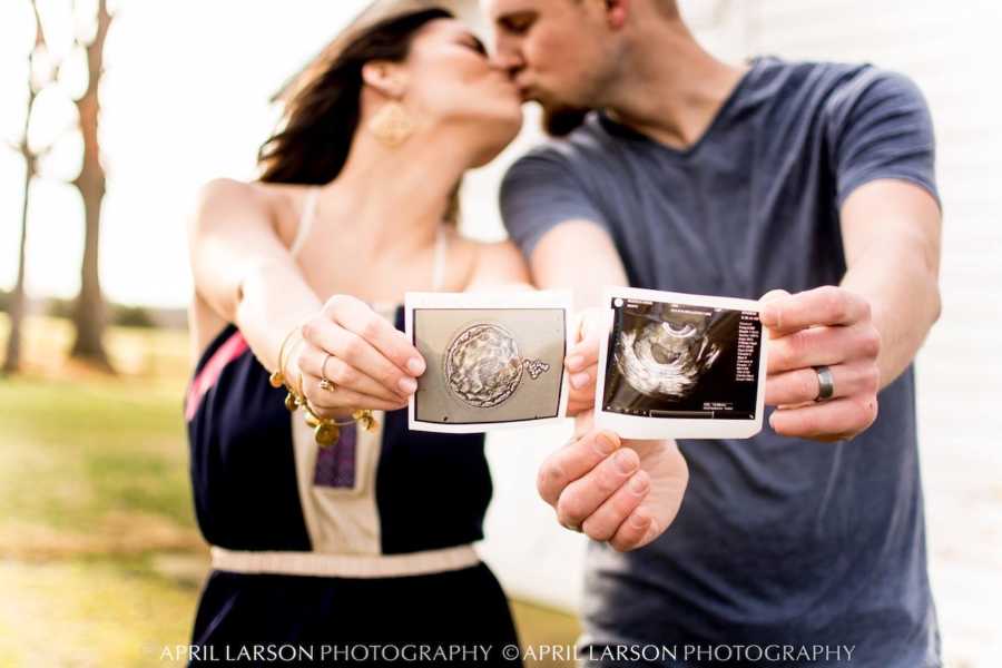 Husband and wife stand outside kissing as wife hold implanted embryo picture and husband holds ultrasound