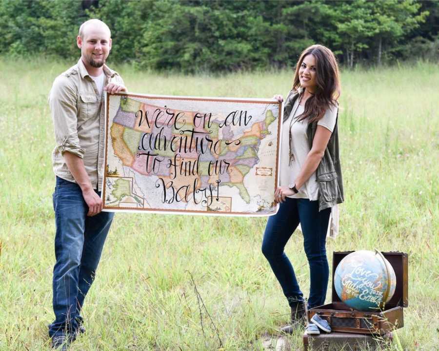 Husband and wife who want to adopt stand outside holding sign that says, "we're on an adventure to find our baby"