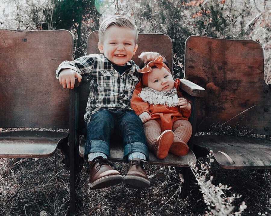 Little boy sits in stadium chair outside with adopted baby sister