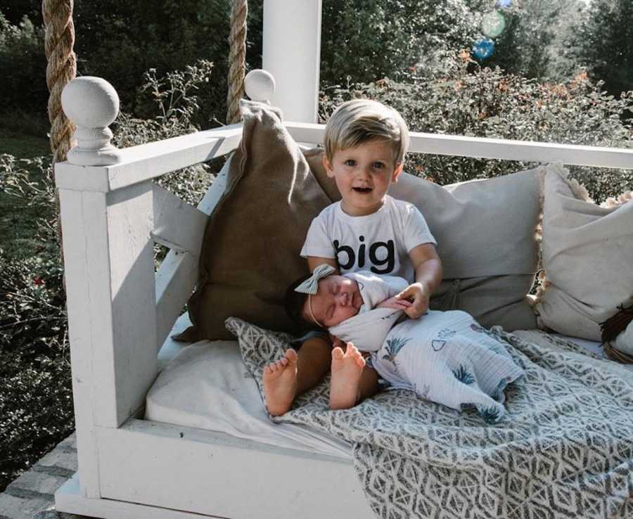 Little boy sits on porch swing holding adopted baby sister in his lap