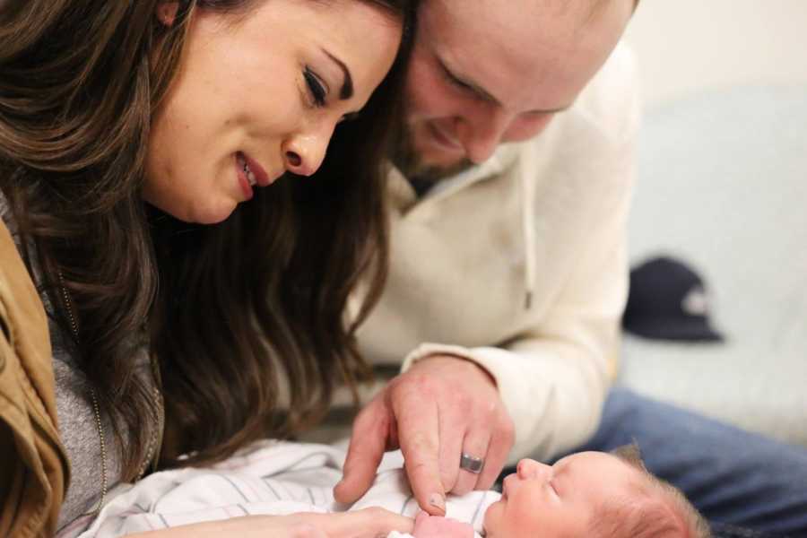 Husband and wife smiles as they look at adopted newborn