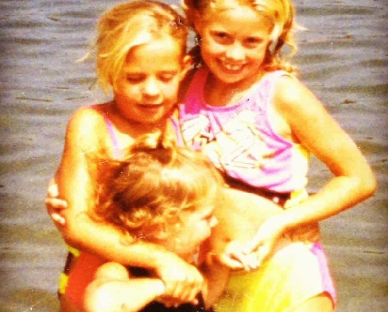 Three sisters stand in swimsuits near body of water as little kids, one has since passed from addiction