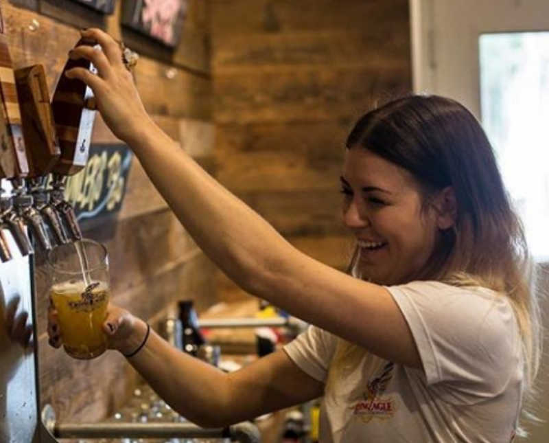 Woman with alcoholism smiles as she fills up glass of beer on tap