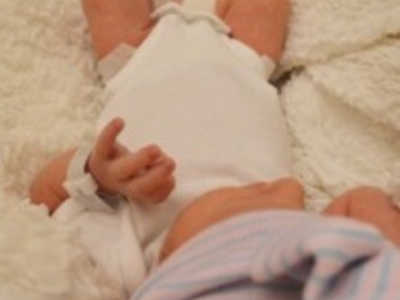 Newborn lays on white blanket with white onesie on