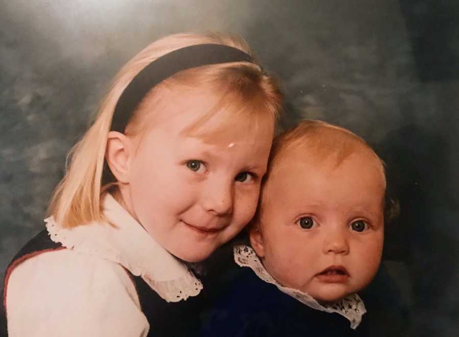 Little girl smiles in photoshoot holding onto baby daughter