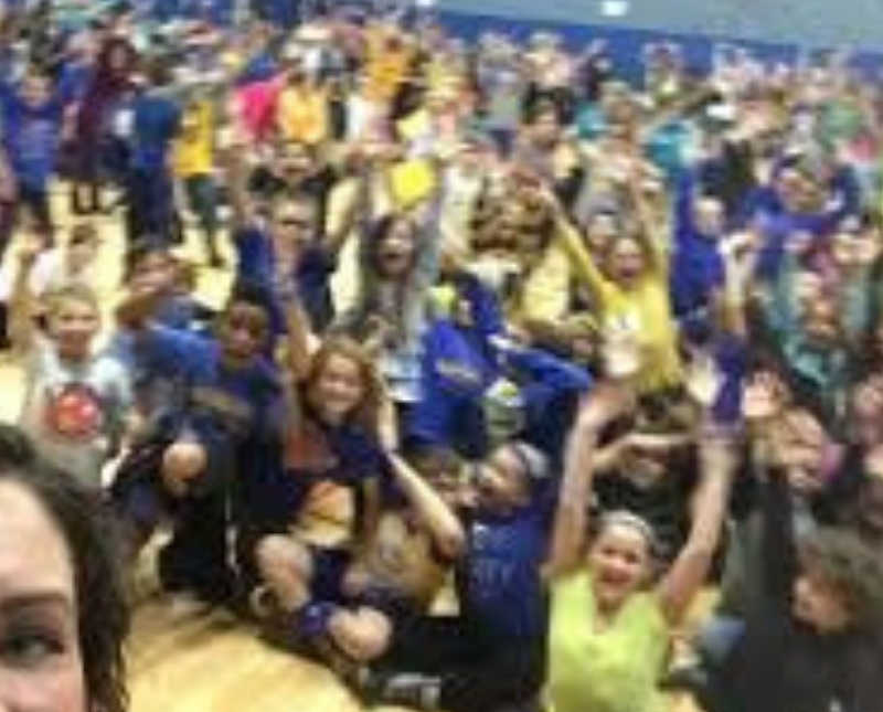 Woman takes selfie with gymnasium full of young children in background