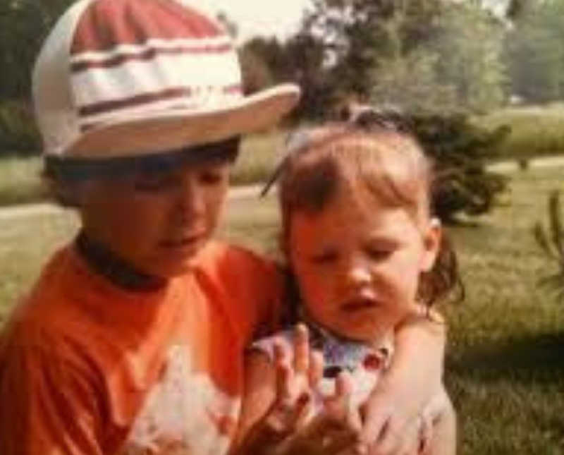 Young boy stands outside with arm around younger sister