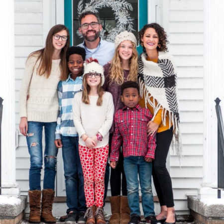 Woman stands outside her home with husband and five kids