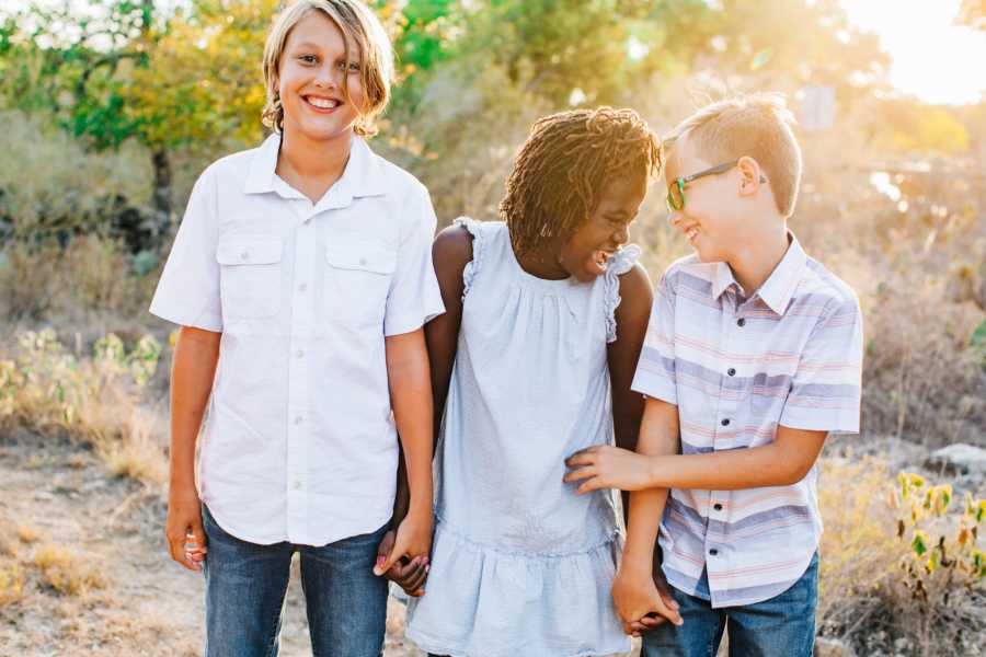 Oldest brother smile as he holds hands with adopted sister who is laughing with other brother