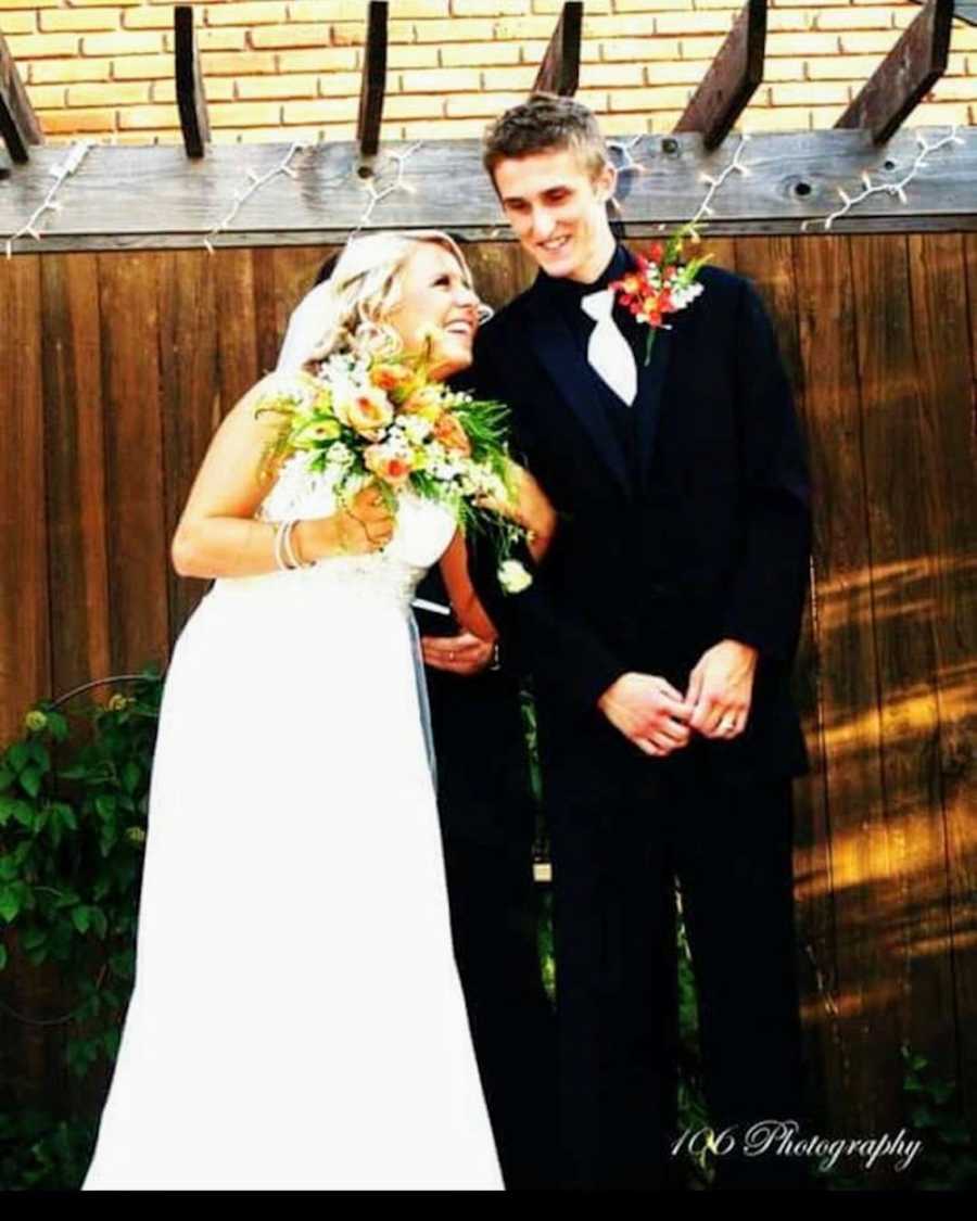 Bride and groom stand smiling under wooden gazebo