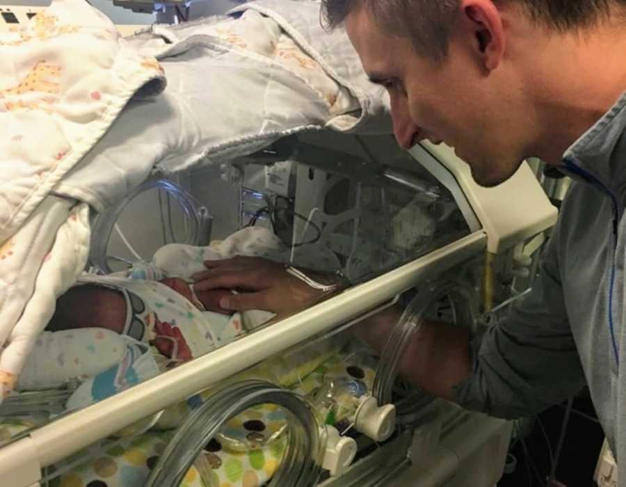 Husband smiles as he touches his adopted newborn in NICU