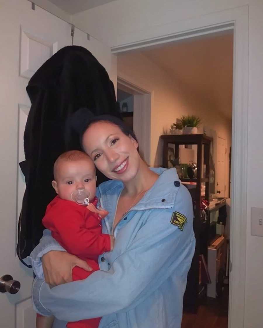 Woman who stopped taking drugs to have child stands smiling in home holding baby boy