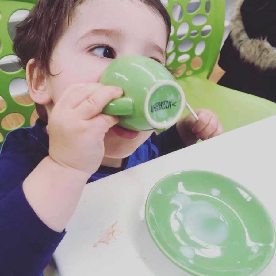 Little boy sits drinking out of little green mug