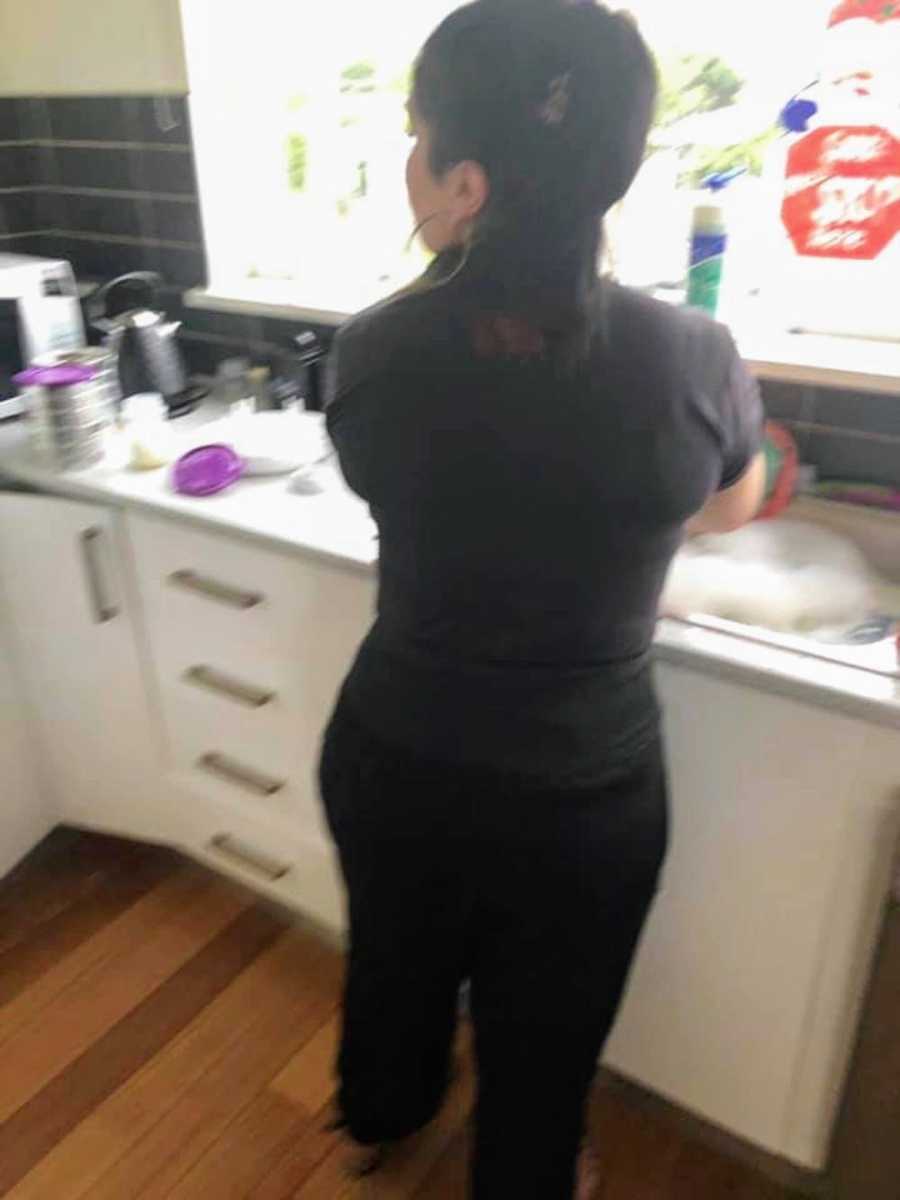 Mother stands at sink washing dishes looking to her side