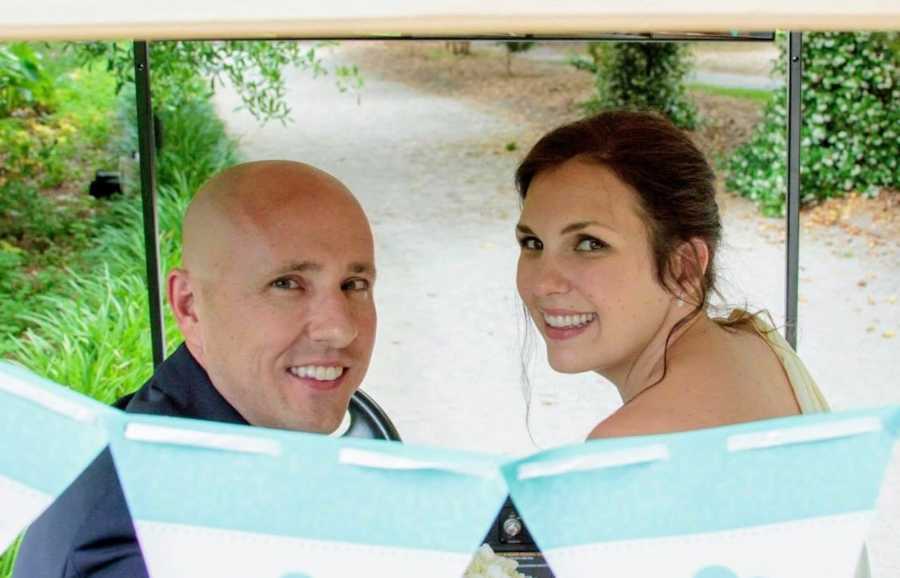 Engaged couple smile over their shoulders as they sit in golf cart