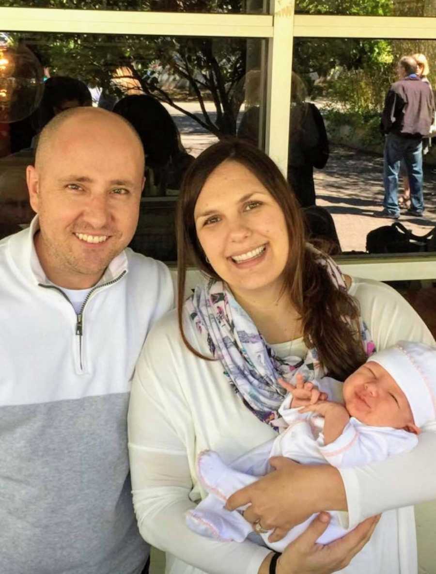Husband and wife who went through IVF treatment stand smiling outside with newborn
