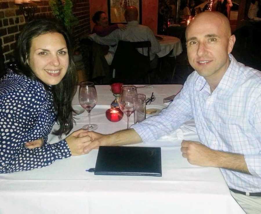 Woman sits at restaurant table smiling while holding hands with man who sits across from her