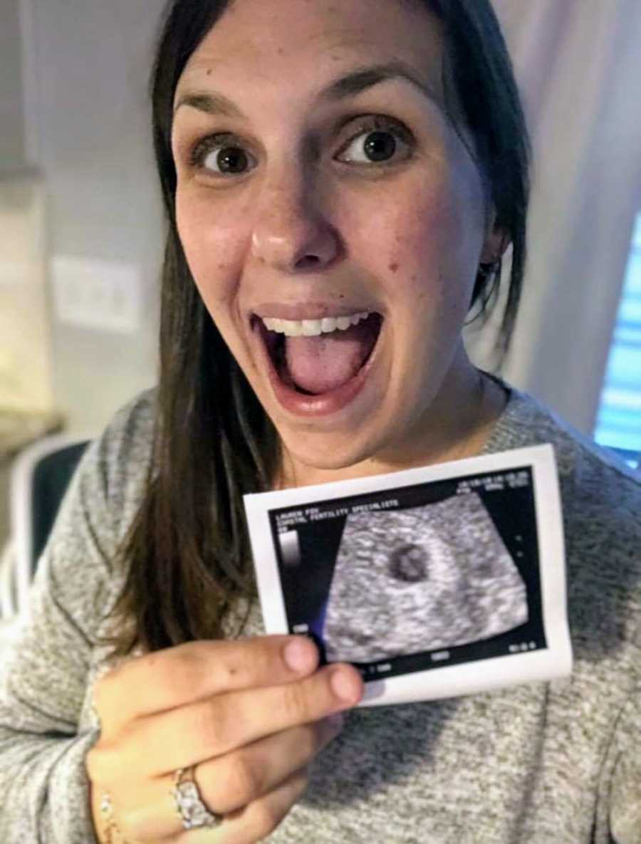 Woman smiles as she holds up picture of ultrasound