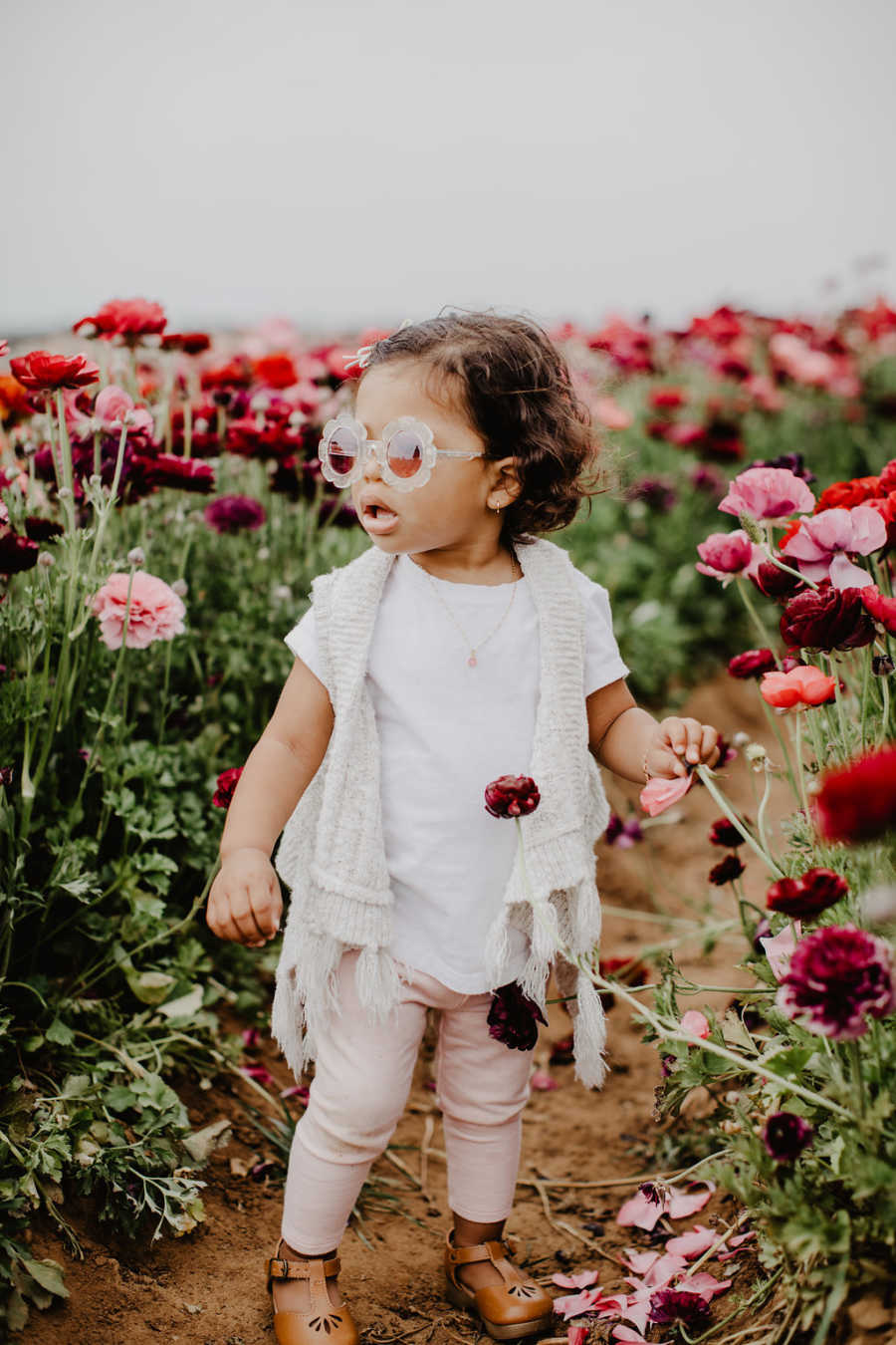 Little girl wearing sunglasses stands in field of pink and red flowers