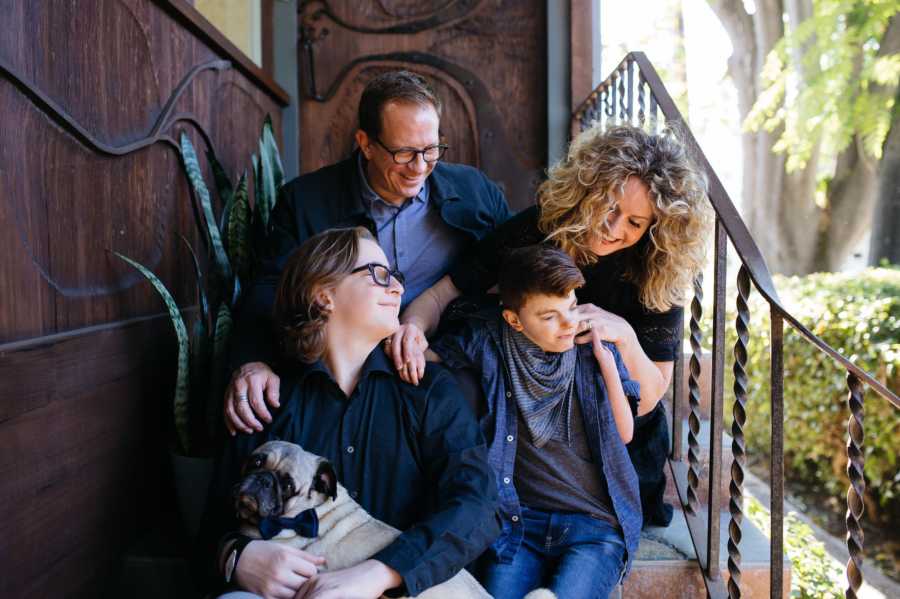 Husband and wife sit on steps with oldest son who holds their dog and youngest with Cornelia de Lange Syndrome