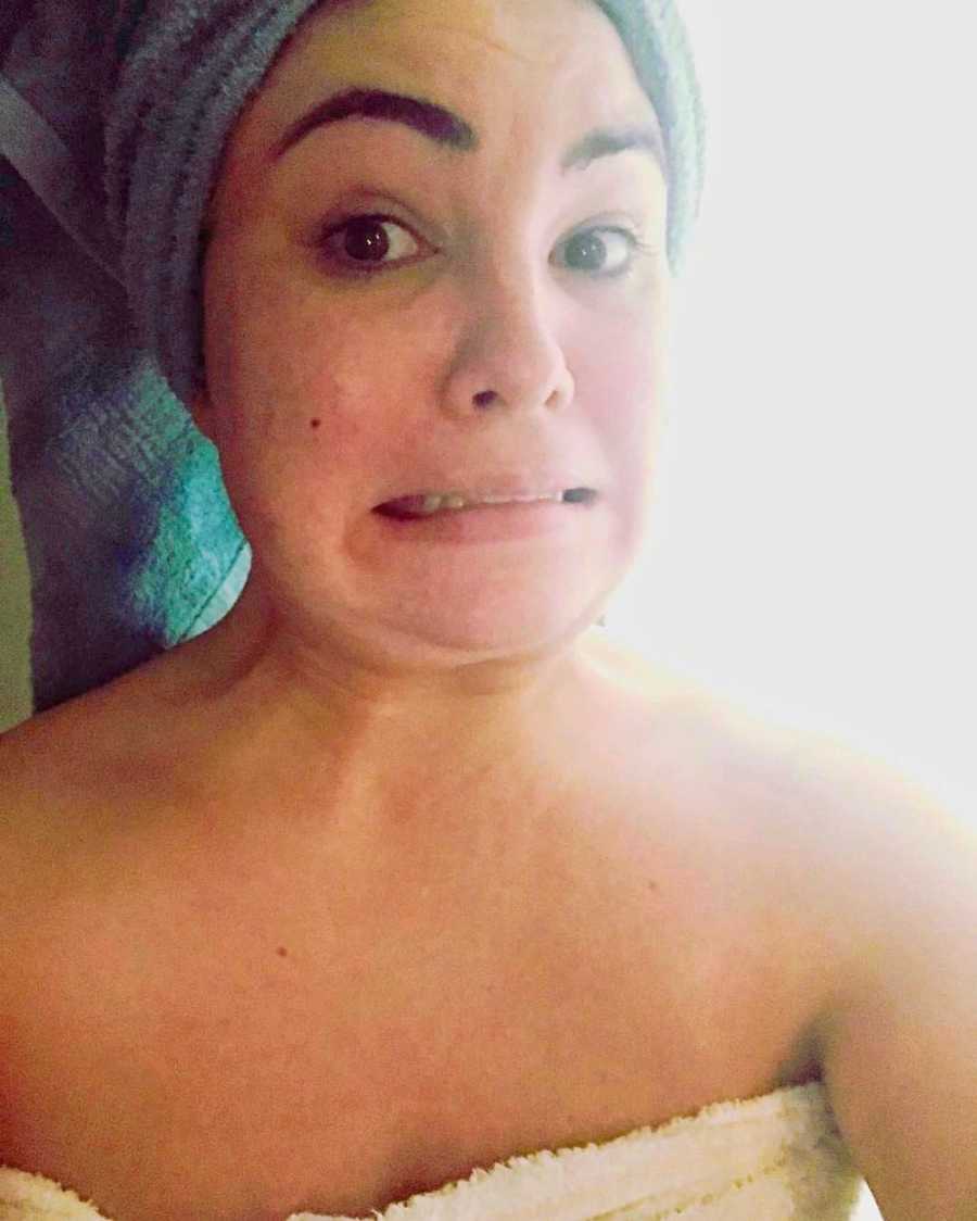 Woman with towel around her body and head makes face in selfie with pimple on her face
