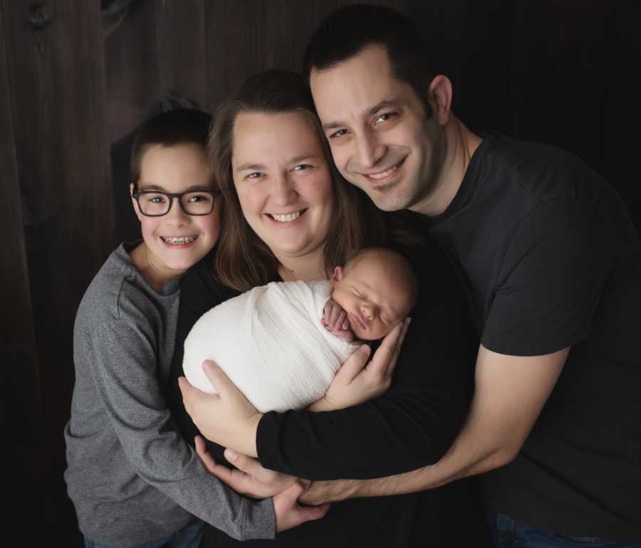 Mother and father pose for family photo with their young son and newborn son
