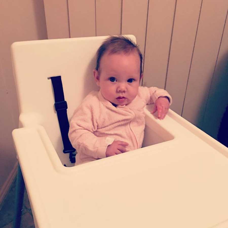 Baby who is home from NICU sits in high chair in light pink onesie