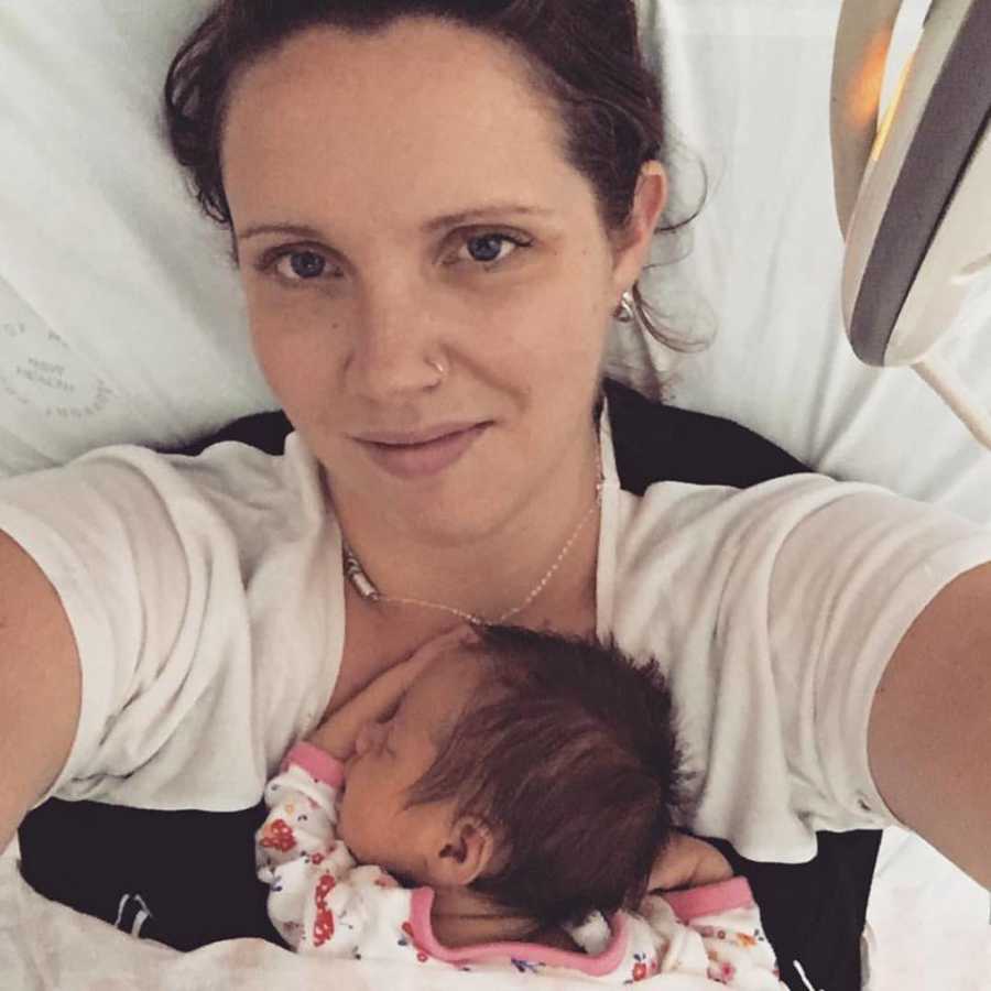 Mother smiles in selfie as he baby daughter lays asleep on her chest