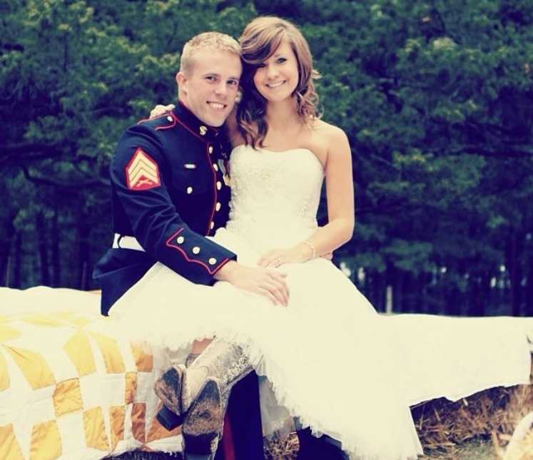 Bride sits on lap of marine groom who sits on hay bales covered in blankets