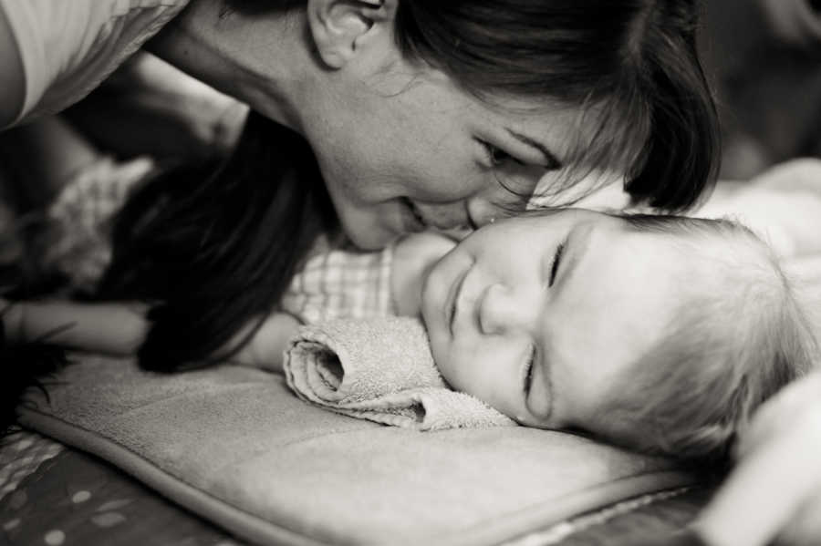 Mother leans over to kiss young daughter who lays on her back