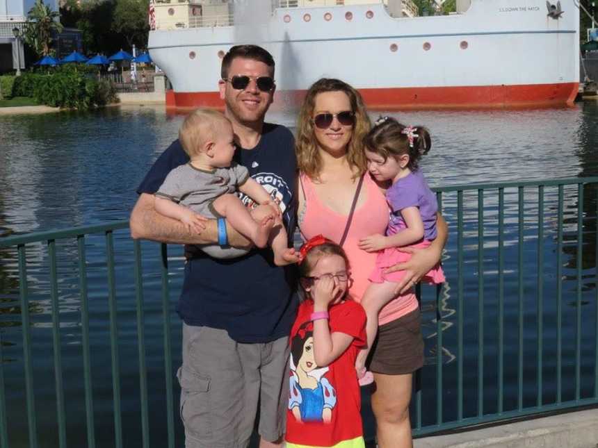 Wife stands holding daughter beside late husband who holds their son while third child stands in front of them