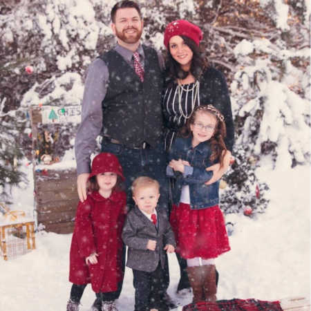 Husband and wife stand outside in snowy weather with their three children