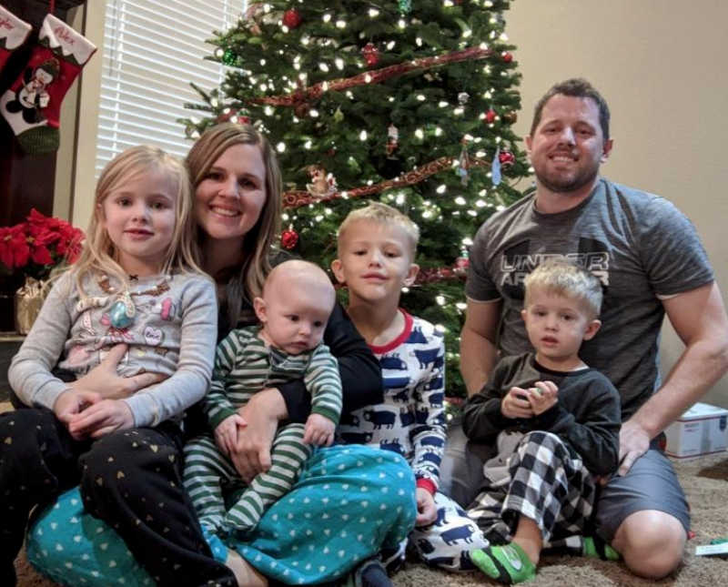 Wife sits with four kids and late husband on floor in front of Christmas tree in their home