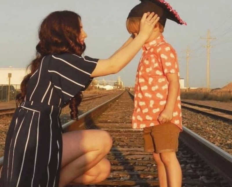 Mother crouches down on train track to put graduation cap on young son's head