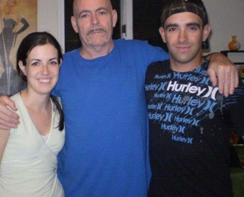 Brother and sister stand smiling with their addict father who has since passed away