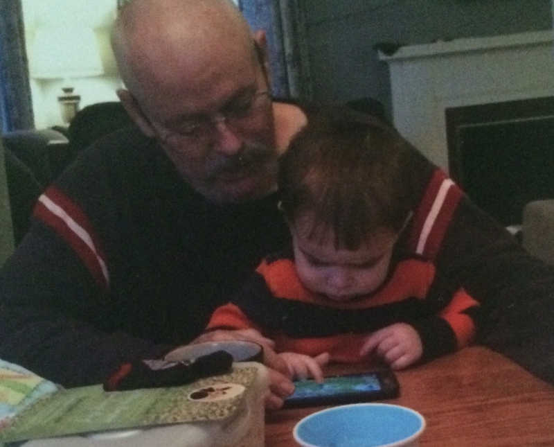 Little boy sits on grandfather's lap who is an addict playing on phone