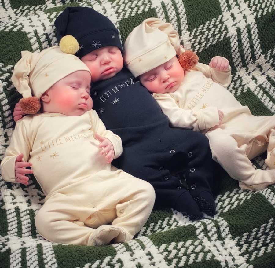 Triplets lay on green and white blanket asleep in pj's and sleep caps