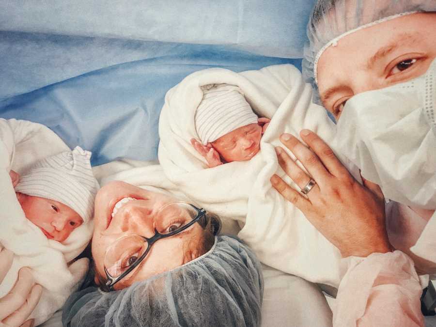 Husband and wife smile as they hold two of their triplet newborns