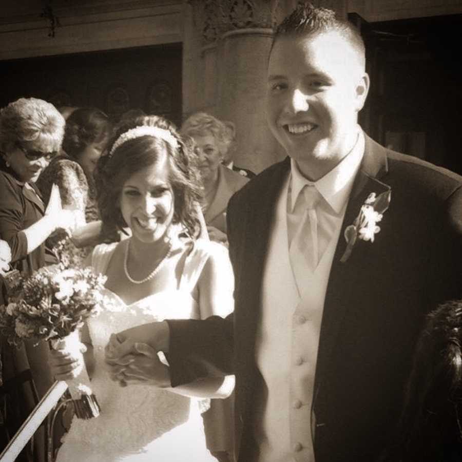 Bride and groom walk hand in hand after their wedding with people smiling in background