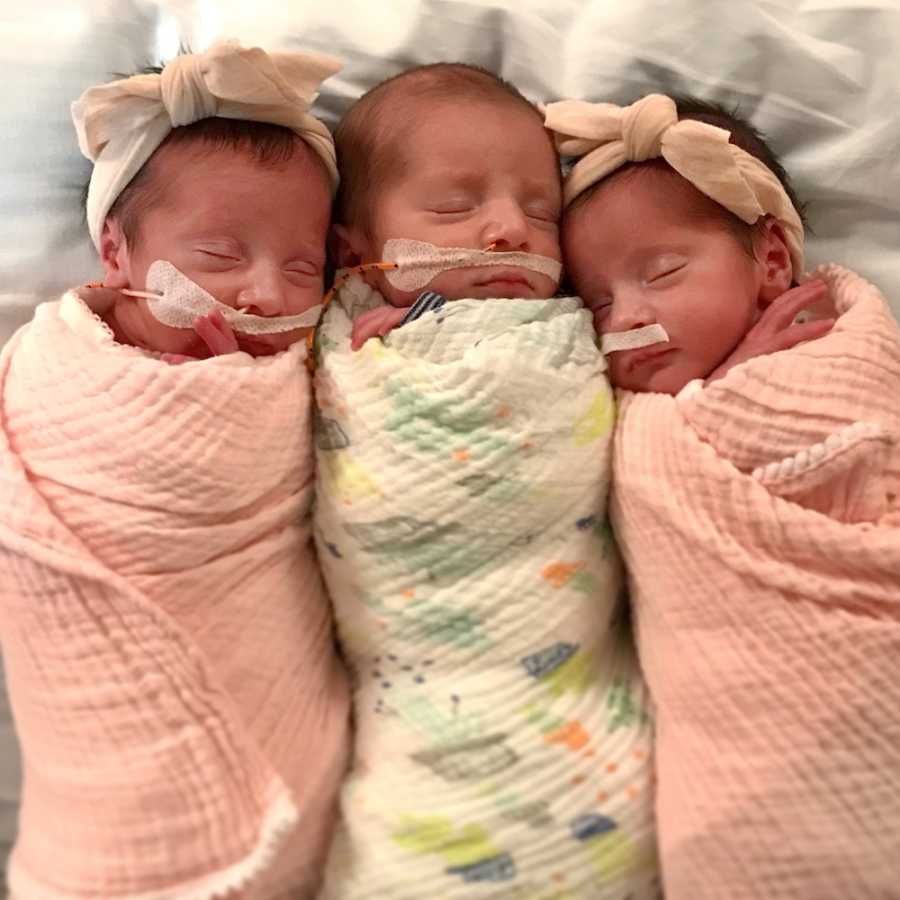 Newborn triplets lay on their backs asleep swaddled in blankets