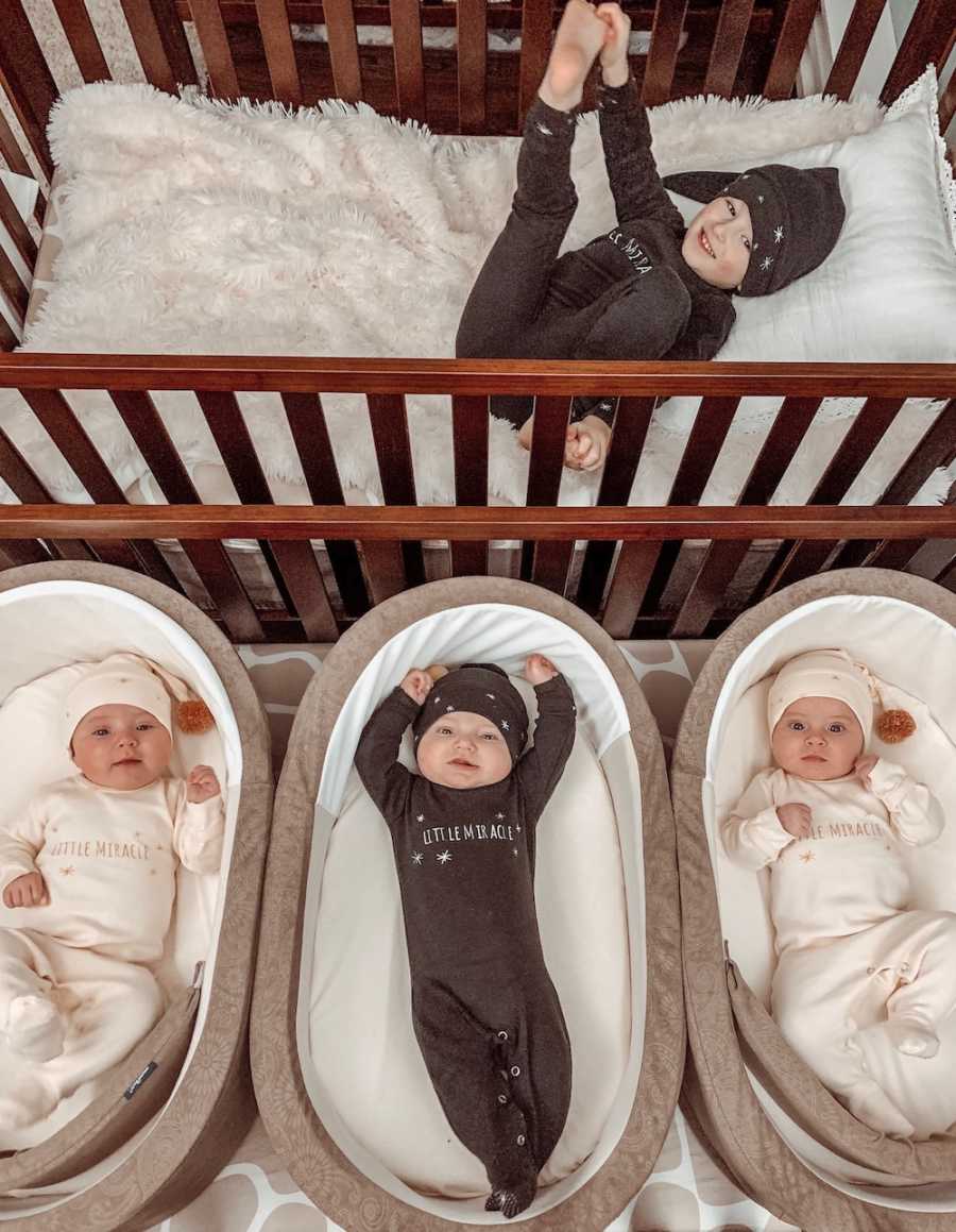 Aerial view of little boy laying in crib with triplet babies asleep in cradles