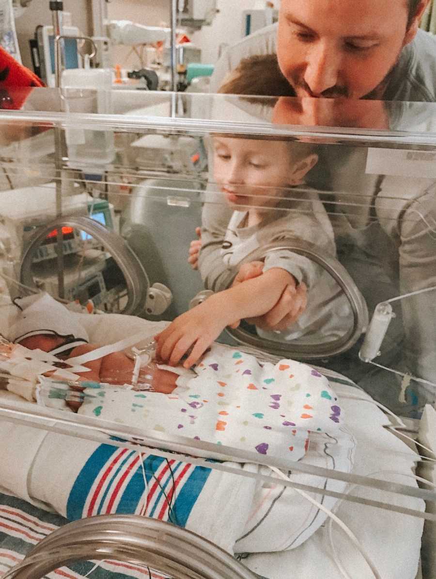 Father stands with son as they look at newborn in NICU
