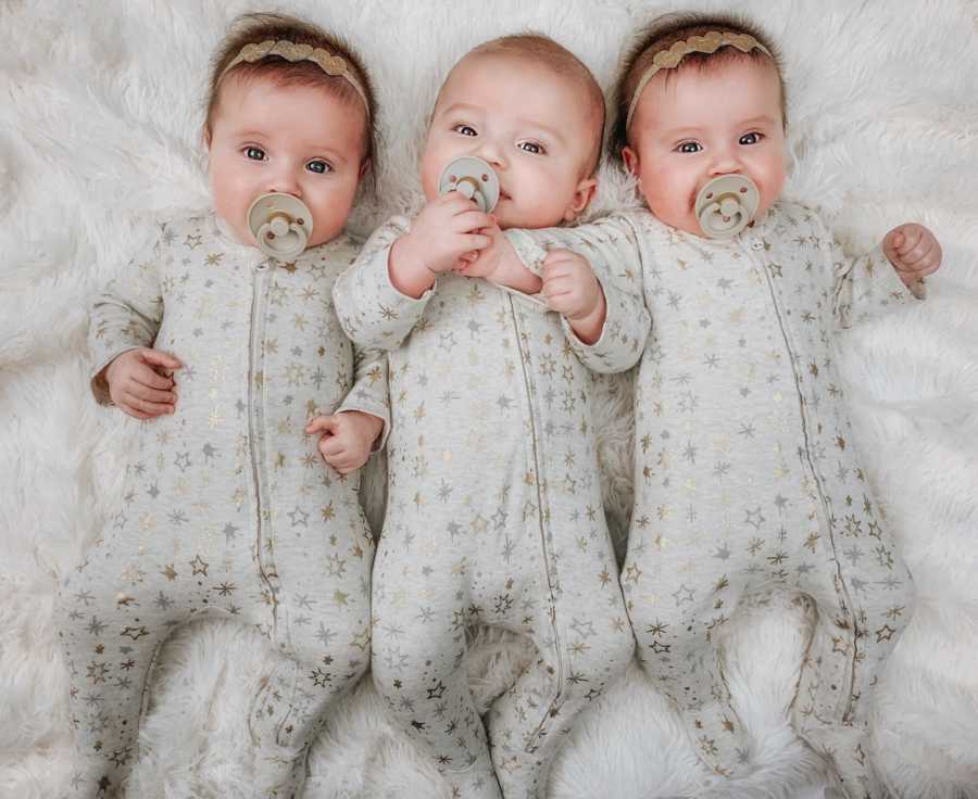 Triplets lay on their back wearing matching gray onesies